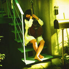 A woman in a white dress sits barefoot on outdoor stairs holding a dark acoustic guitar, with a green-tinted warm light illuminating the scene.