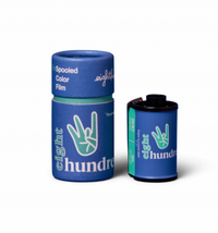 Two cylindrical containers of 35mm color film, one with the film spooled and the other standing upright. Both have blue branding with white text and graphics.