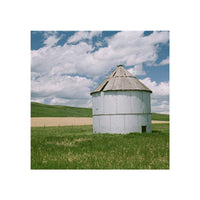White grain silo in a grassy field under a blue sky, captured with the soft, natural aesthetic of FLIC Fusion 200 film.