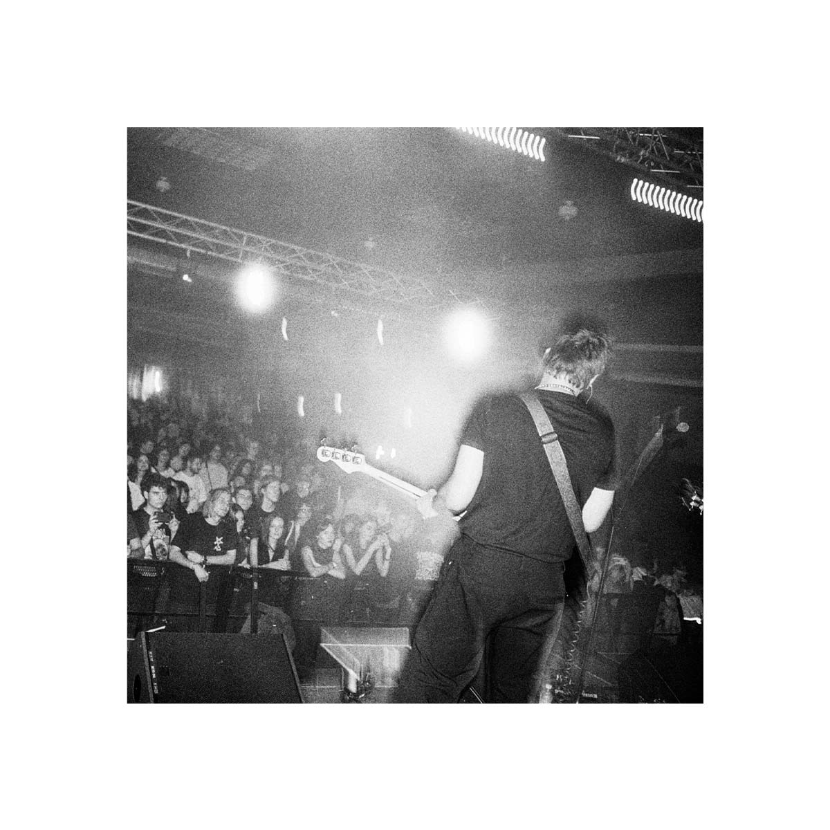 Black and white concert scene shot on 35mm film, showing a bassist performing on stage before a crowd with high contrast.