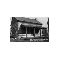 Black and white landscape shot of a rustic log cabin with a porch, captured on FPP Let It Snow 100 35mm film.
