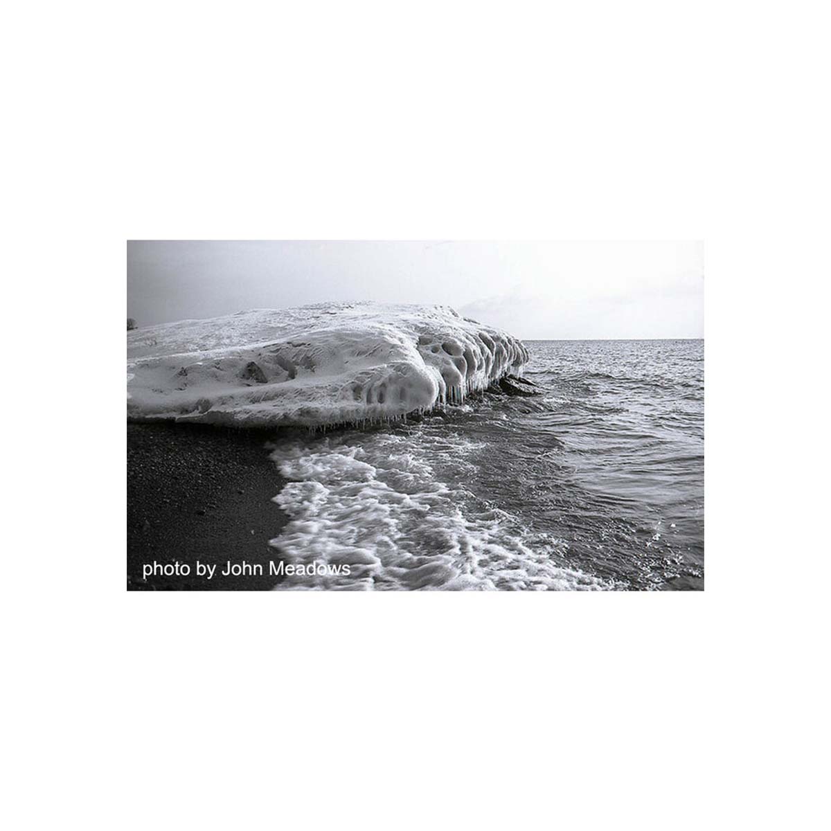 Black and white landscape shot of an icy shoreline with frozen rock formations and ocean waves, captured on 35mm film.