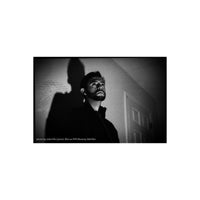 Black and white portrait photograph of a man looking upward, with a dramatic shadow cast on the wall behind him. Small text at the bottom reads 'photo by Jake Fife (@lord_fife) on FPP Mummy 400 film'.