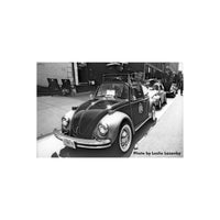 High-contrast black and white street scene featuring a vintage Volkswagen Beetle parked on a sunny city sidewalk.