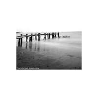 Black and white long exposure of a wooden pier over a smooth, misty ocean shoreline.