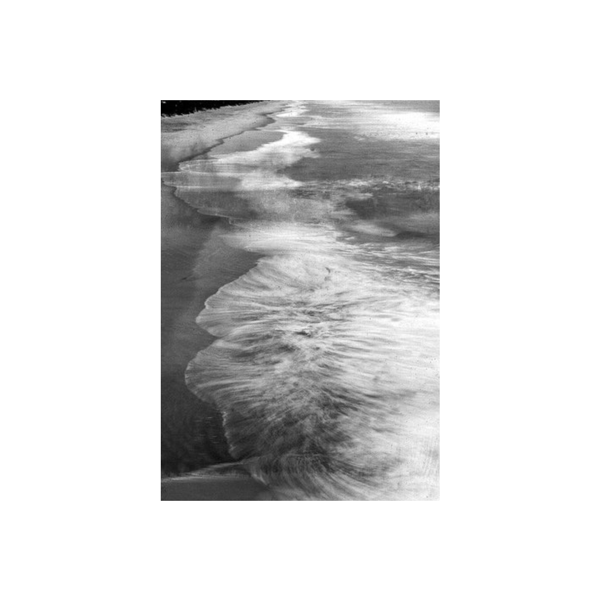 Black and white long exposure of ocean waves washing onto a sandy beach, captured on fine-grain 35mm positive film.