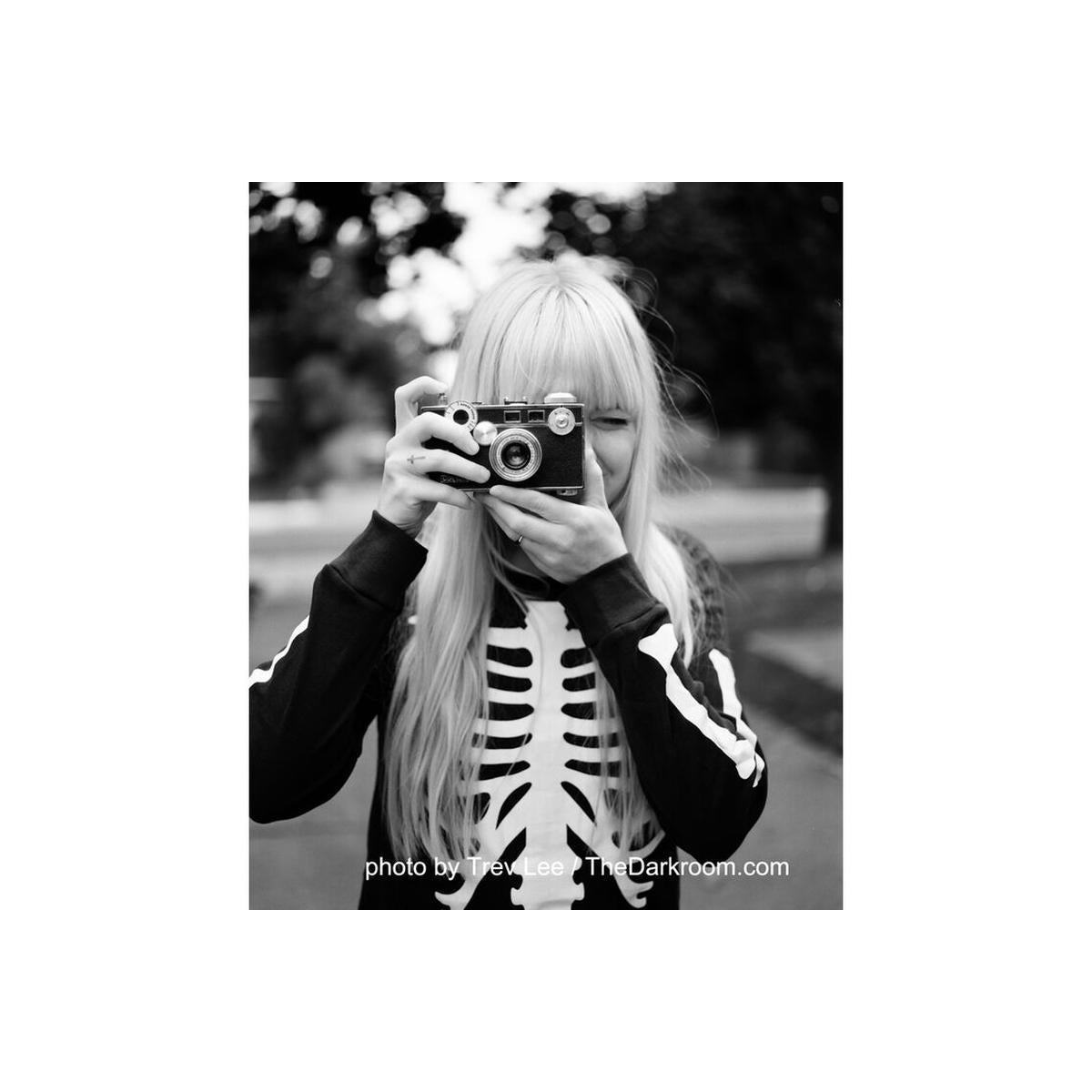 Person in a skeleton sweater holding a vintage camera, captured in high-contrast black and white 120 film style.