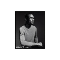 A black and white portrait photograph of a man wearing thick-rimmed glasses and a gray turtleneck sweater, seated against a dark studio background. White text in the lower-left corner reads 'photo by Tariq Tarey'.