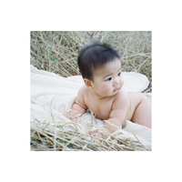 A baby lying on a white cloth in dry grass, captured with the warm, grainy aesthetic of FilmNeverDie UMI 800 color film.