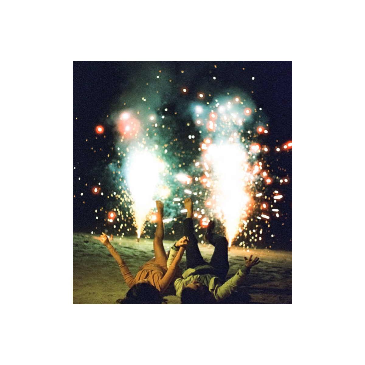 Two people lying on a beach at night with bright fireworks, captured on grainy 35mm color film.