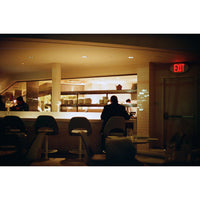 Dining area with patrons and a counter inside a restaurant, featuring an 'EXIT' sign.