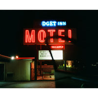 A nighttime photograph of a lit 'Budget Inn Motel' neon sign, with a dark car silhouette in the foreground and a white border at the top and bottom.