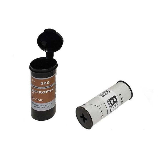 Two film canisters for a camera, one standing upright with its black flip-top lid open and showing a brown label, and one lying on its side with a white label and black end caps, photographed on a plain white background.