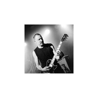 Black and white photo of a man playing an electric guitar on stage under dramatic spotlighting.
