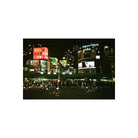 A nighttime city scene with brightly lit billboards and signs, including visible text such as AlpenTokyo and Japanese signage, with a crowd of people crossing a street in the foreground. The image has decorative sparkle/star overlays.