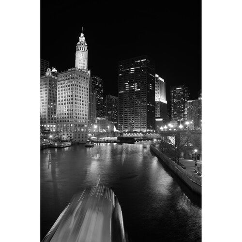 Black and white cityscape at night with illuminated buildings and a river.