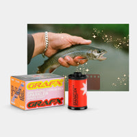 Grafx Sparkler 56mm color negative film shown with its orange and white retail box and a red film canister, alongside a sample of a fish photo edited with sparkly overlays and a small brown color card on a light gray background.