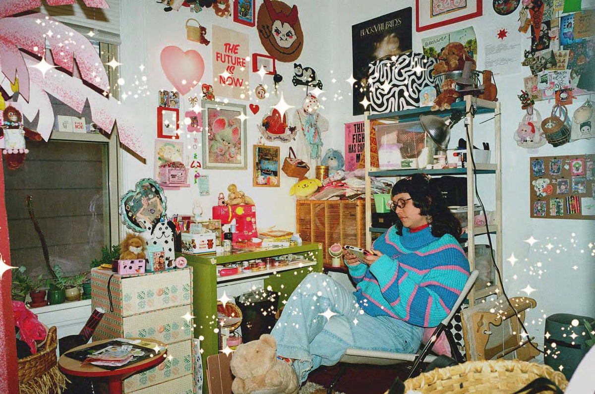 A cozy, cluttered room decorated with pink and red heart motifs, posters, and shelves, featuring a person sitting in a chair wearing a colorful striped sweater and light blue jeans.