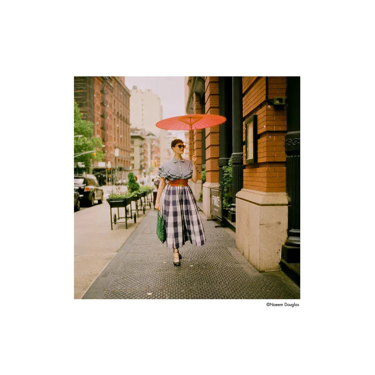 Woman in a plaid dress and red parasol walking on a city sidewalk, captured with HARMAN Phoenix II 200 color film.