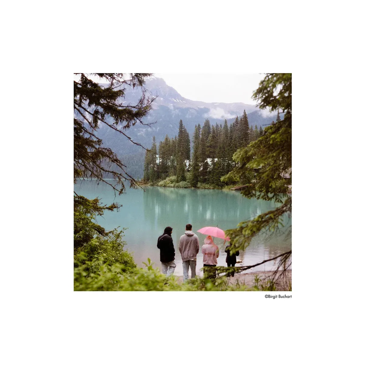 Four people standing by a turquoise mountain lake, captured with the distinct, punchy color tones of Harman Phoenix II film.