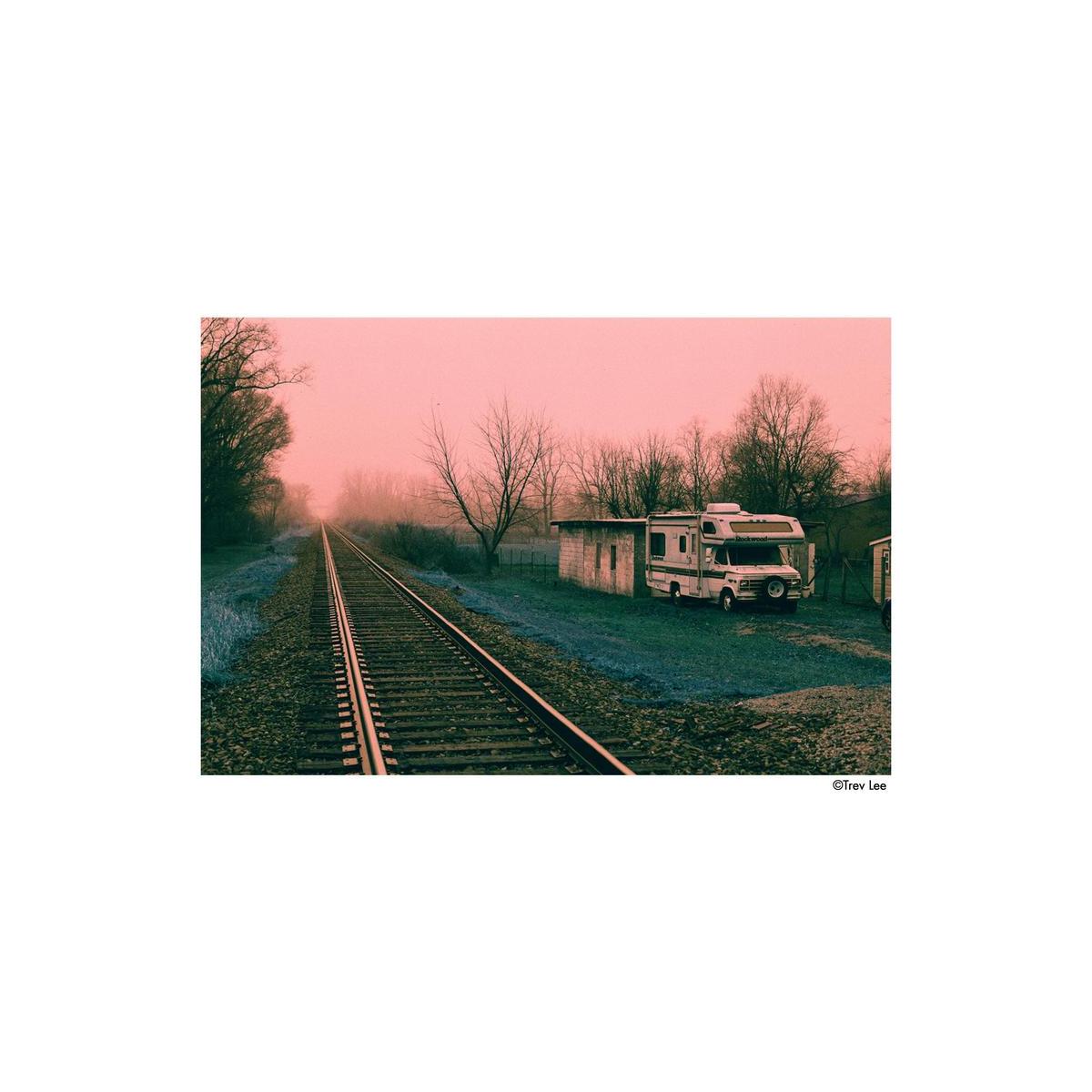 Vintage RV parked near train tracks with a pinkish sky