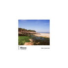 A square photographic print showing a coastal shoreline with rocky tide pools, green seaweed-covered rocks, a pale sandy beach, and blue sky, presented on a white page with the text 'PHOENIX ISO 200 COLOUR FILM' and 'Photo: Hannah Gross'.