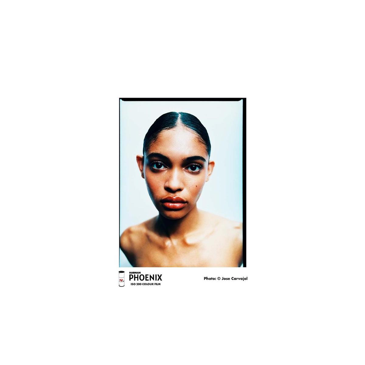 A framed fashion portrait print featuring a close-up of a woman with dark hair parted down the middle, set against a light blue background. The print is presented with a black frame on a white background, with 'HARNESS PHOENIX' branding and 'Photo: © Jose Carvajal' printed below the frame.