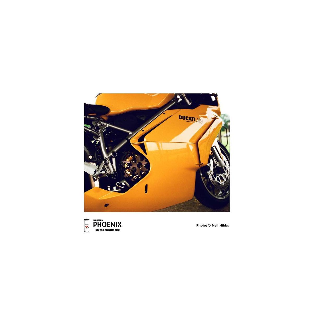 A close-up photograph of a bright orange Ducati motorcycle body panel and engine, with visible branding including 'DUCATI' and 'PHOENIX' at the bottom of the print.