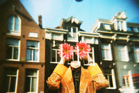 Lo-fi Holga 135FC film photo showing a person in a plaid blazer holding pink flowers against a backdrop of city buildings.