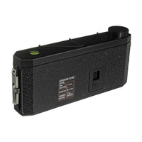 A black textured exposure guide camera accessory with a circular dial, a small green indicator light, and a printed exposure chart label on the side, shown against a plain white background.