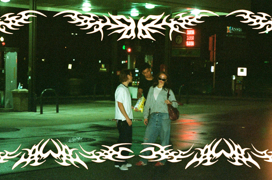 Three people standing at night outside a convenience store under green and red store lights, with a white tribal graphic border overlaying the top and bottom of the photo.