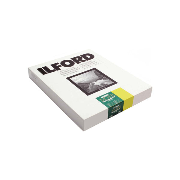 A boxed Ilford photo paper pack shown at an angle on a plain white background. The white box features the Ilford logo in black, a black-and-white sample photograph, and a green-and-yellow paper strip wrapped around the side.