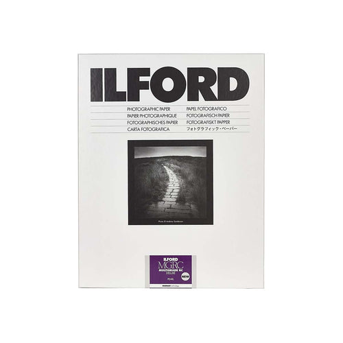 A pack of Ilford B&W (black and white) fine grade photographic paper, featuring a white cover with bold black text, a central black and white sample photograph of a path, and a purple Ilford logo sticker at the bottom.