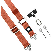 An orange-brown nylon sling strap set with silver metal hardware, shown on a white background with included accessories: a black quick-release patch, a carabiner clip, and two small metal tools. The strap has embossed branding and a visible KODNIK logo patch.