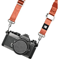 Orange Kodak multipurpose camera strap with quick-detach buckles and silver hardware attached to a black vintage camera.