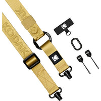 A tan Kodak camera strap with black hardware, shown alongside its included accessories: a black branded loop, a black carabiner clip, and two black threaded screw tools. The strap features embossed 'KODAK' lettering and a black brand patch.