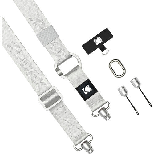 A Kodak camera strap in light gray with silver metal hardware, shown alongside a black branded keeper, a carabiner, and two small silver tools on a plain white background.