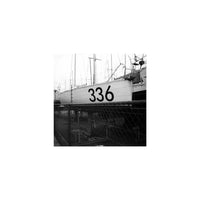 Black and white film photograph of a sailboat hull marked 336, seen through a chain-link fence with grainy texture.