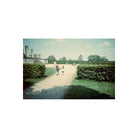 Two people walk down a garden path in this 35mm film shot featuring deep, cool tones and moody, experimental colors.