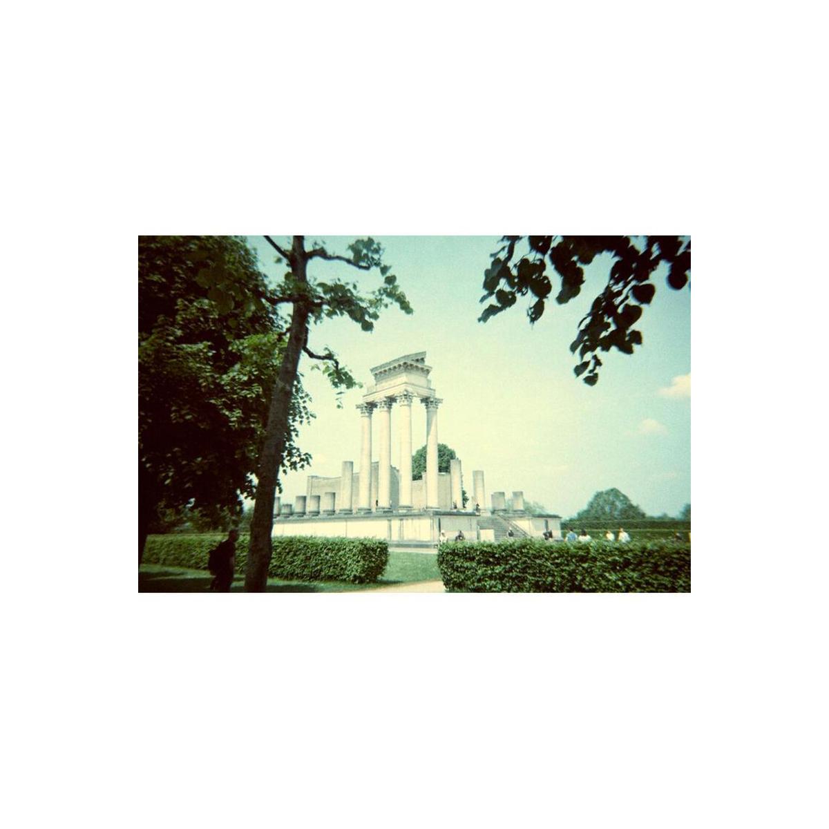 Classical stone temple in a park, captured on 35mm film with moody, cool-toned colors and a vintage experimental aesthetic.