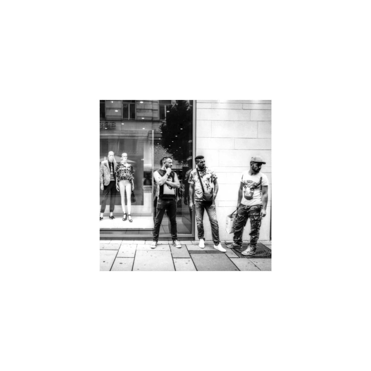 High-contrast black and white street photography shot on KONO! Rekorder film showing three men standing by a storefront.
