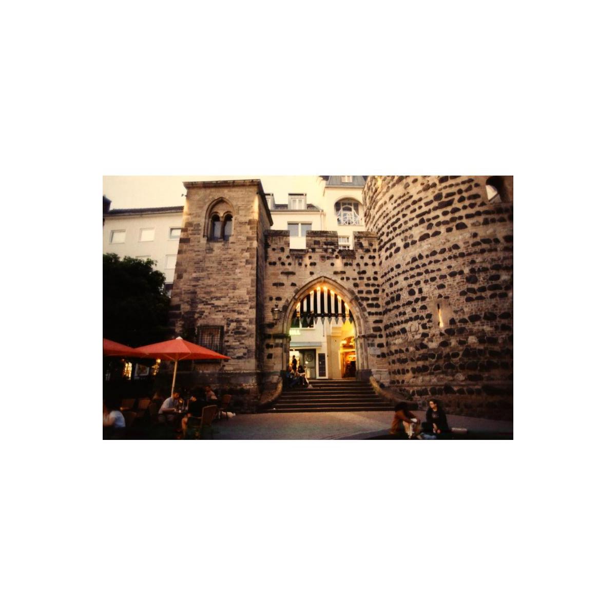 Analog street photography of a historic stone archway and tower with warm lighting, captured on KONO! Smile 200 color film.