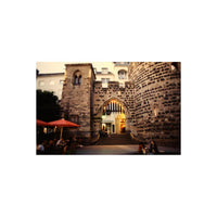 Analog street photography of a historic stone archway and tower with warm lighting, captured on KONO! Smile 200 color film.
