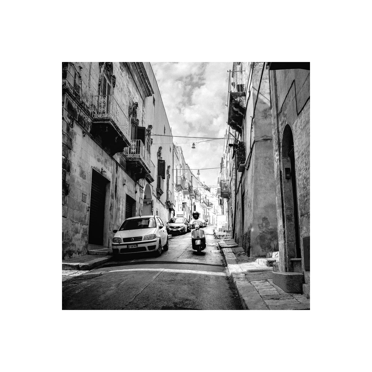 Black and white street scene featuring a scooter and car on a narrow stone road, captured with Kentmere Pan 100 film.