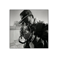 Black and white image of a man with a ball cap look thru a vintage camera with twin lenses