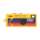 Yellow Kodak Charmera keychain digital camera with a retro 1987 striped graphic design and a compact rectangular body.