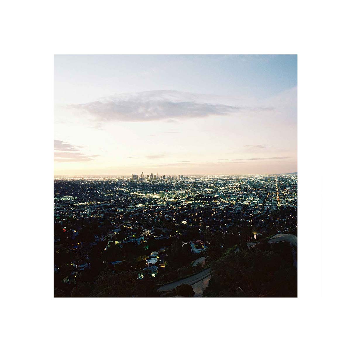 A square art print depicting an aerial view of a sprawling city skyline at dusk, surrounded by a wide white border.