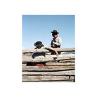 Two people in hats leaning on a rustic wooden fence against a clear blue sky, captured on Kodak Portra 160 color film.