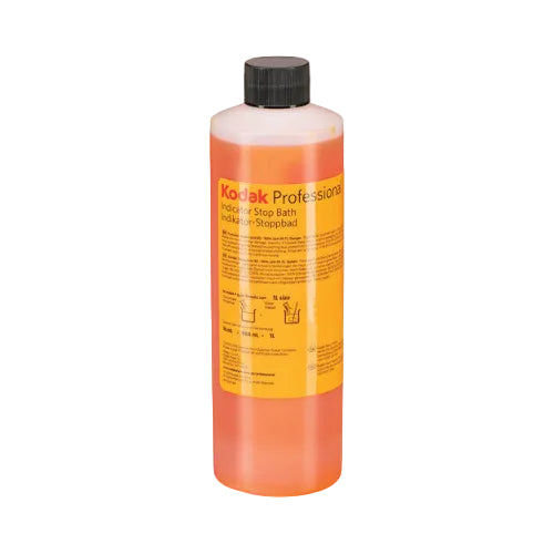 A bottle of Kodak Professional Indicator Stop Bath liquid with orange liquid inside, a yellow label, and a black cap, shown on a white background.