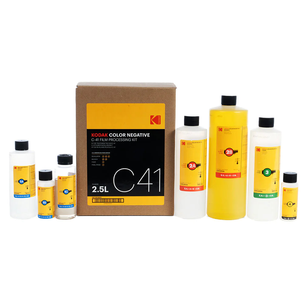 Kodak Color Negative C41 Film Processing Kit with a brown cardboard box and multiple bottles of developer, stop, and fix solutions arranged on a white background.